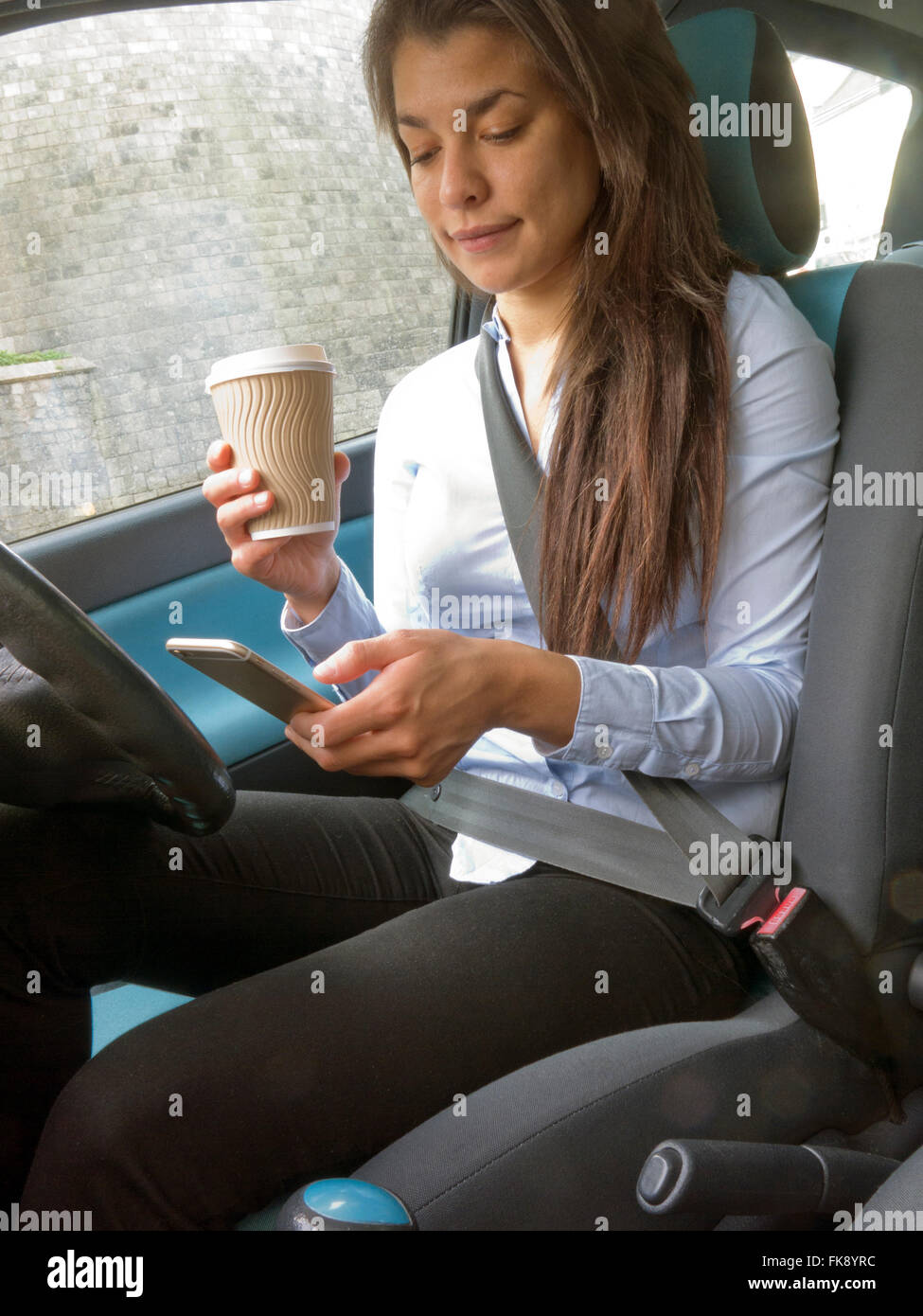 Young woman in car with coffee cup lu son i-phone Banque D'Images
