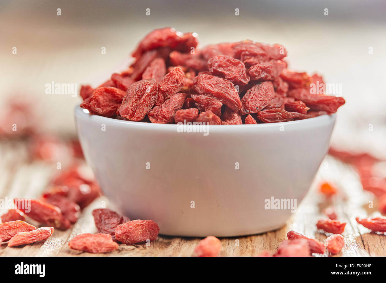 Les baies de Goji super aliment avec des antioxydants, des minéraux et des vitamines dans un bol blanc de chine sur une table en bois brun Banque D'Images