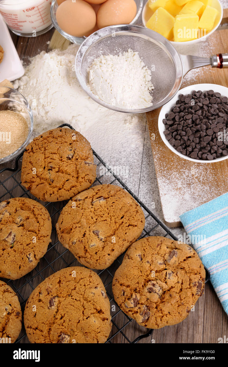 Des cookies aux pépites de chocolat sur une table en bois sombre avec la farine saupoudrée et ingrédients. Banque D'Images