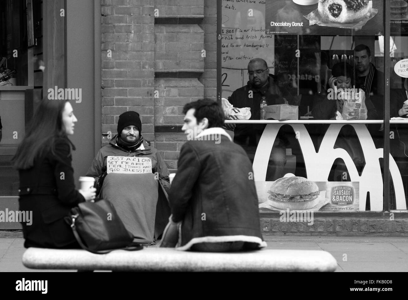 Deux personnes assis et boire tout en un sans-abri est assis à côté d'un restaurant Mcdonalds dans Oxford Street, Londres, Angleterre Banque D'Images