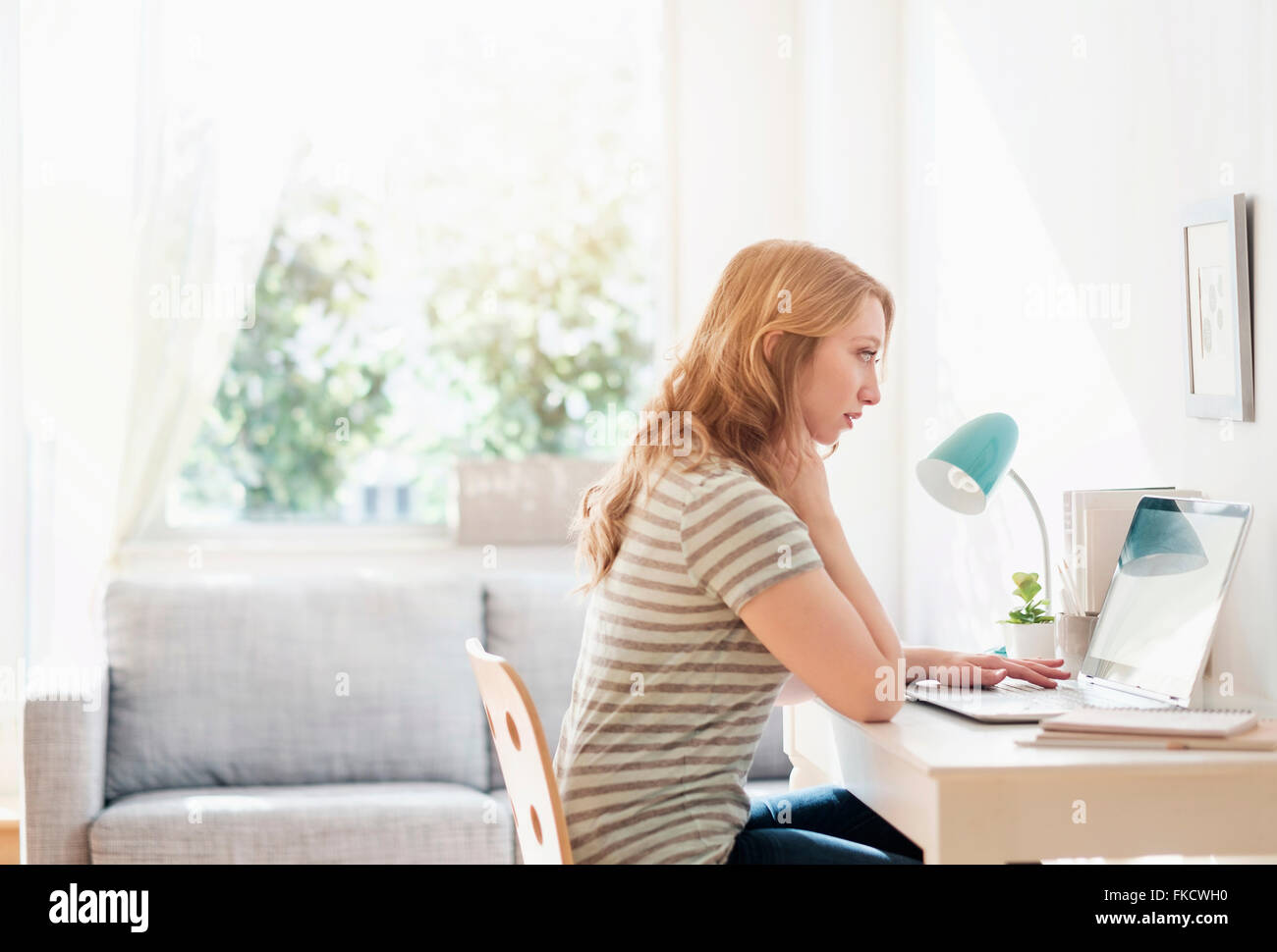 Side-view of young woman working on laptop at home Banque D'Images