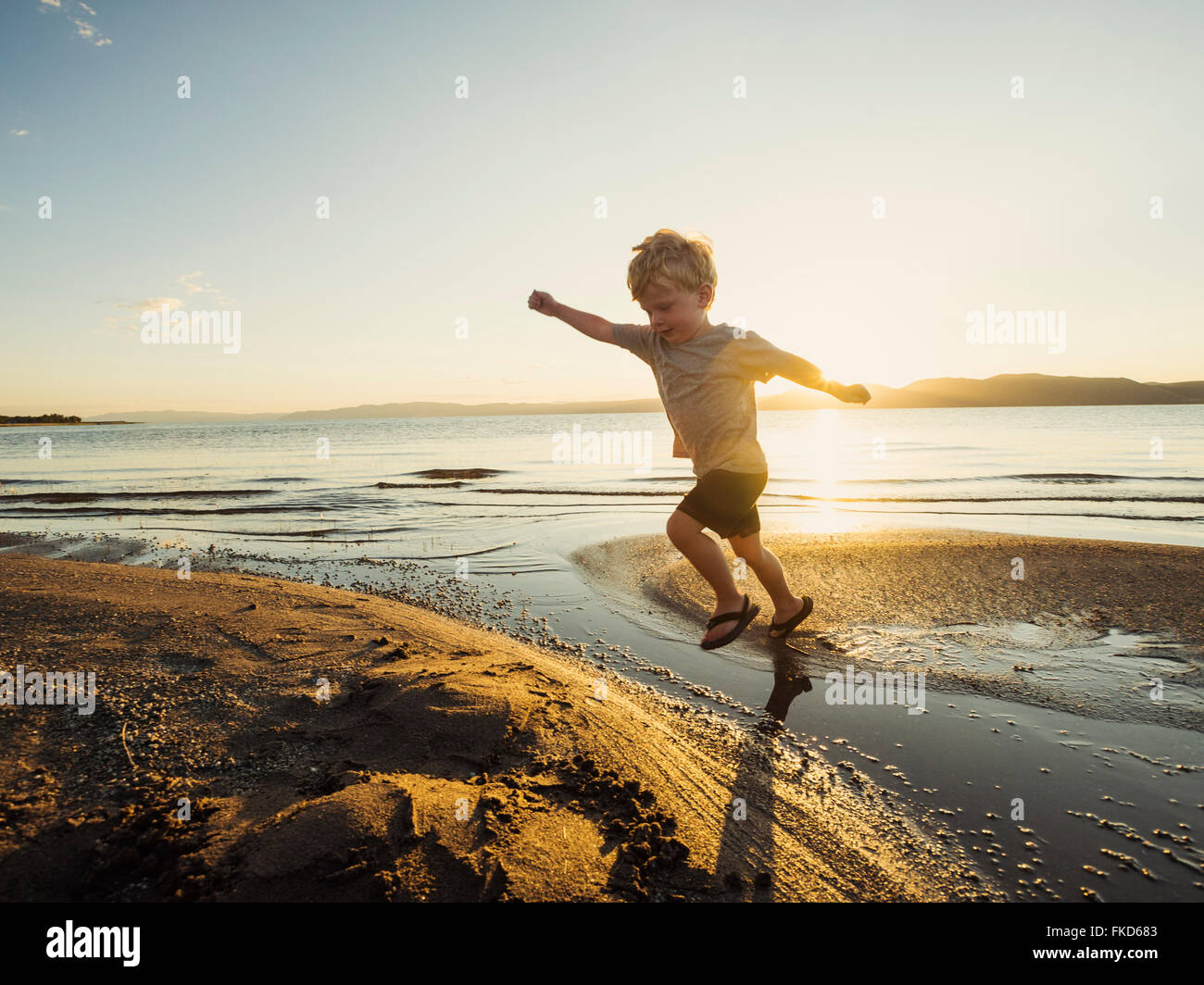 Petit garçon (4-5) saute au-dessus de l'eau sur sunny day Banque D'Images