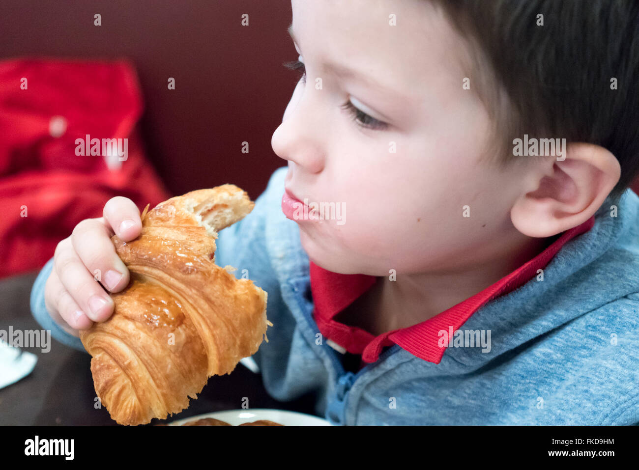 Cute little boy eating croissant Banque D'Images