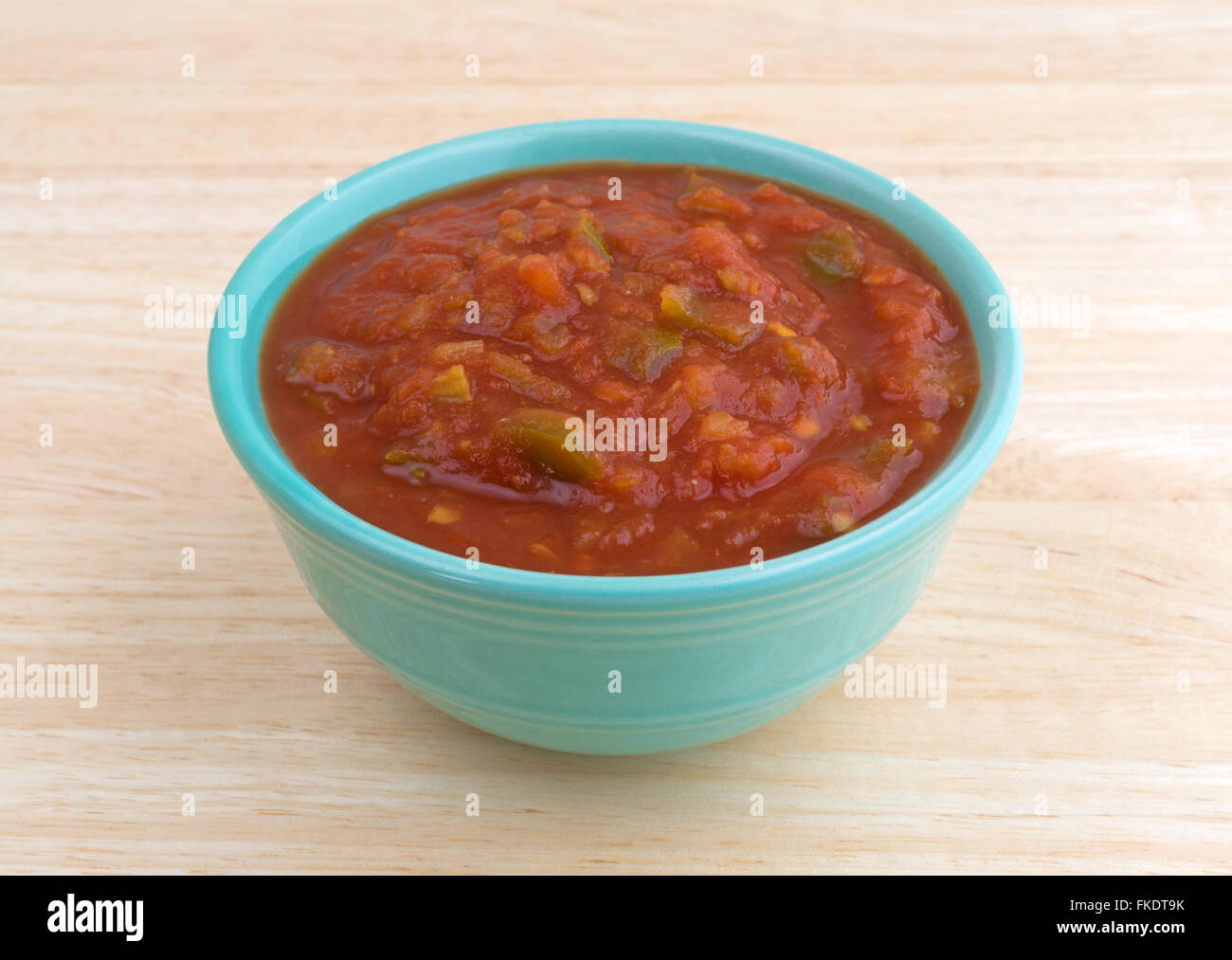 Vue latérale d'un bol de sauce salsa épicée chunky sur un fond en bois éclairé par la lumière naturelle. Banque D'Images