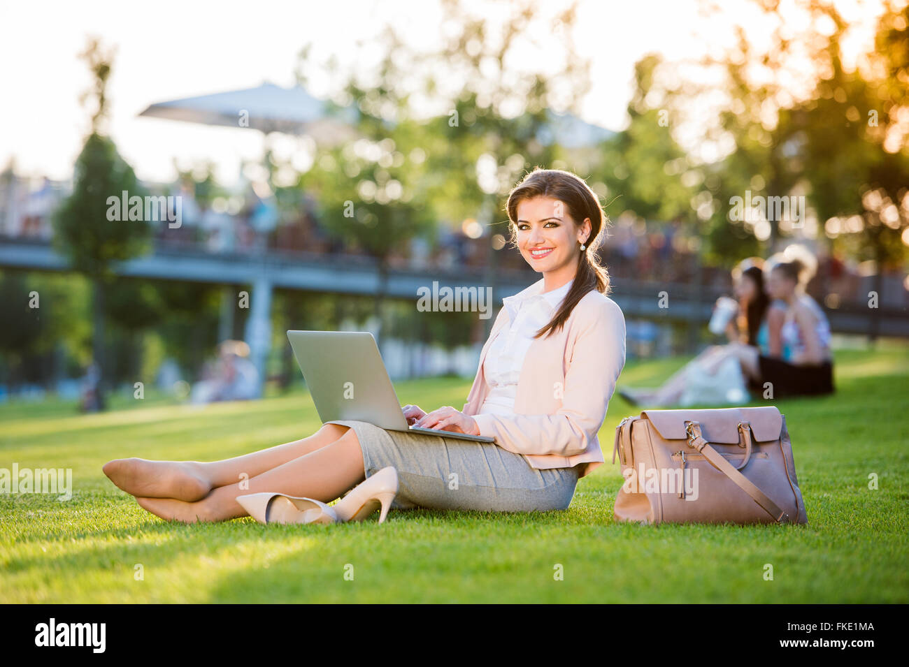 Businesswoman sitting in park working on laptop, sunny summer da Banque D'Images