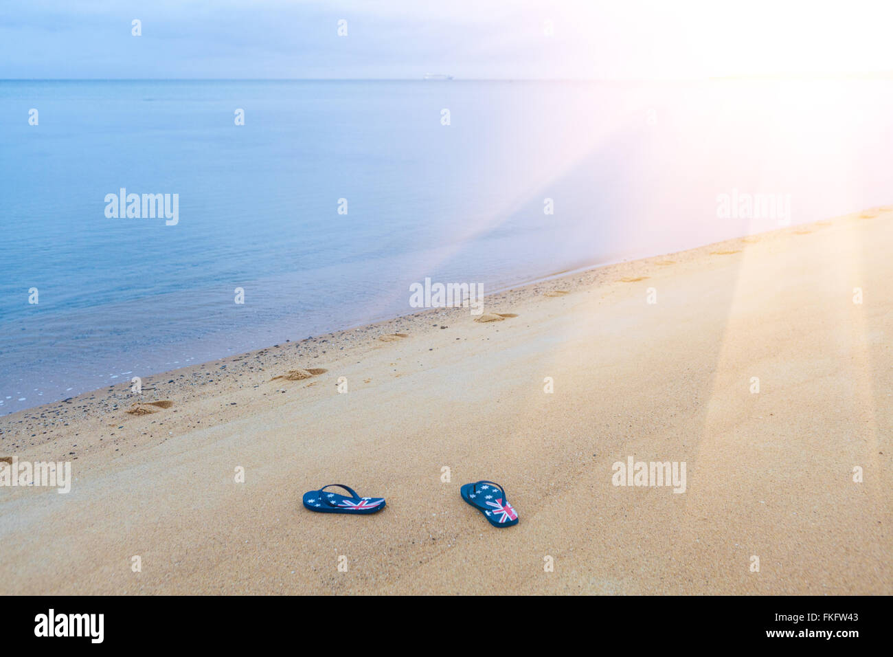 Tongs avec drapeau australien portant sur une plage de sable fin avec soleil Banque D'Images