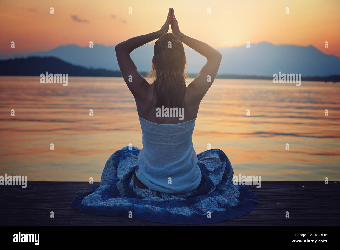 +Femme au coucher du soleil, heure de méditation en face d'un lac . Position de Yoga Banque D'Images