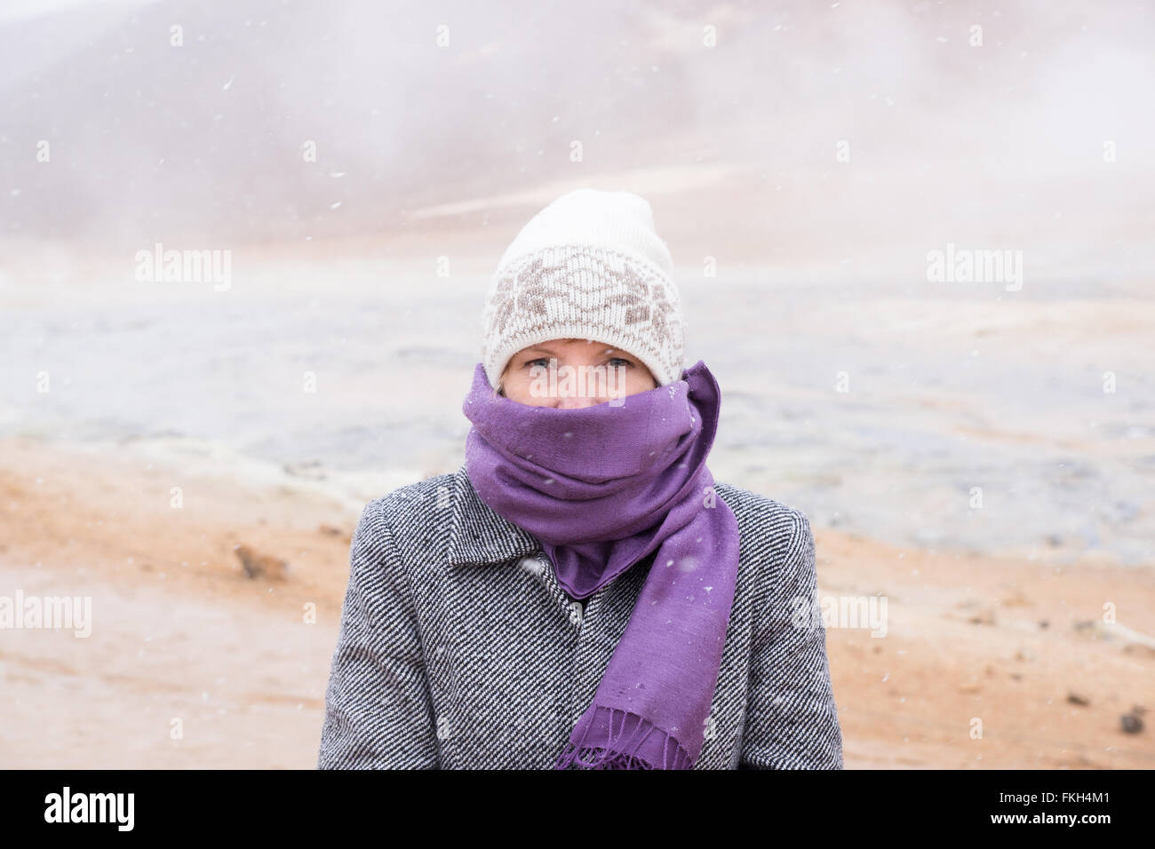 Femme dans la neige avec écharpe et bonnet avec l'Islande sources chaudes à Hverir en arrière-plan Banque D'Images
