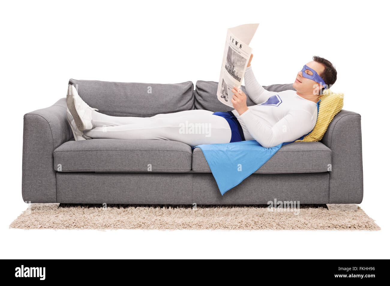 Super-héros jeunes détendue couché sur un canapé gris et lire un journal isolé sur fond blanc Banque D'Images