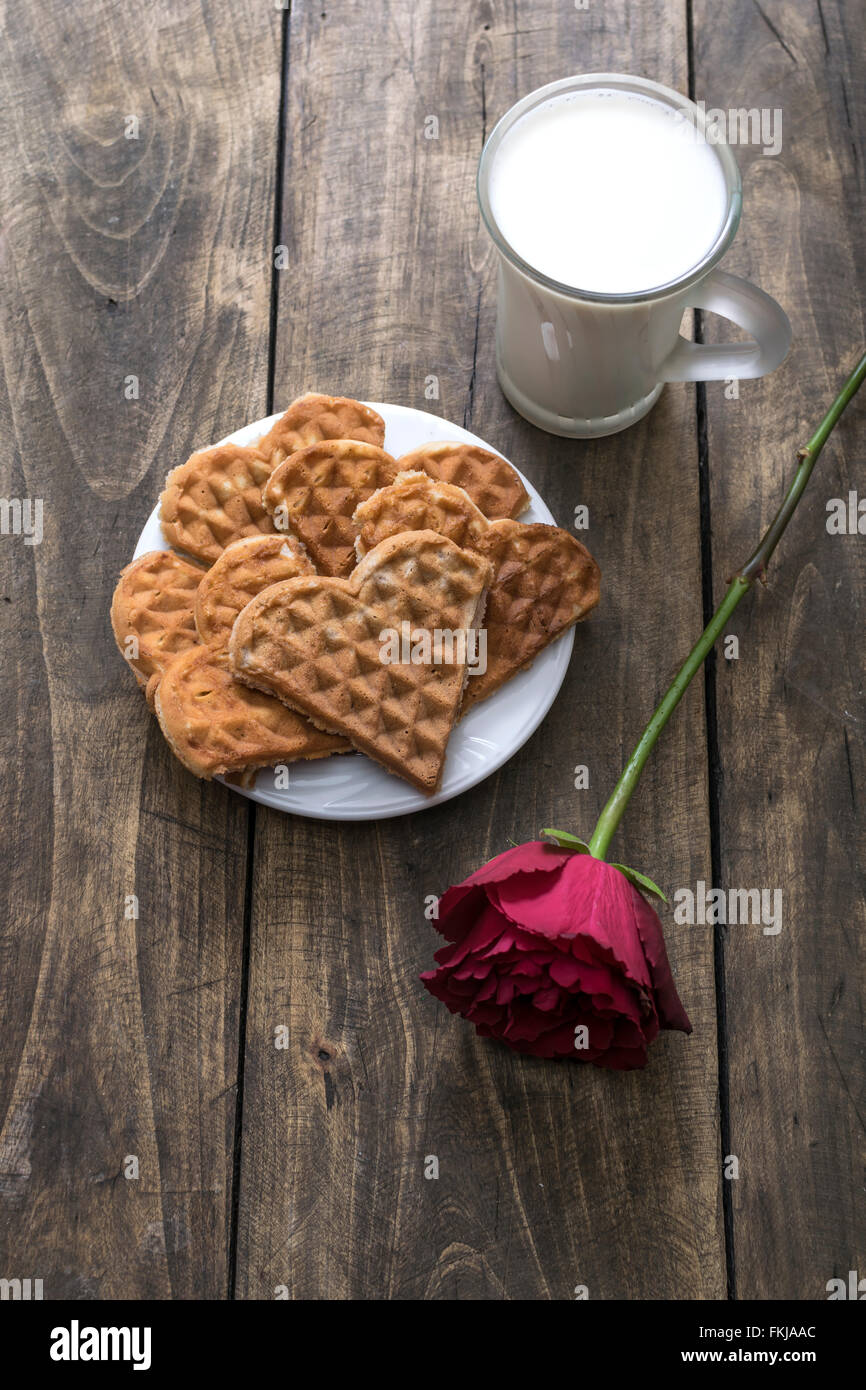 Gaufres en forme de coeur, de lait et de rose rouge sur la table Banque D'Images