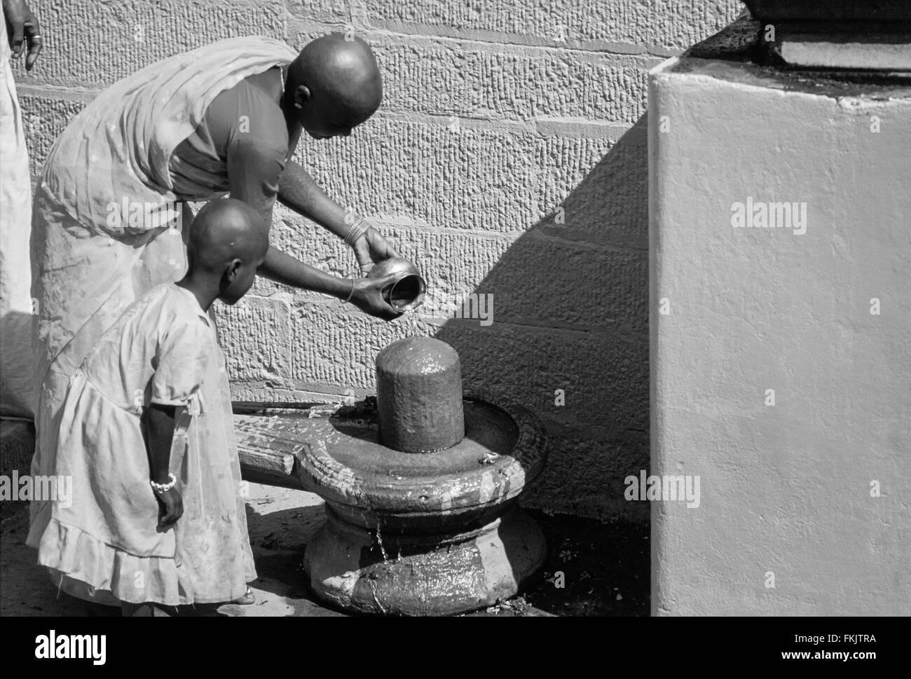 Tête rasée pèlerins hindous,mère et fille de verser de l'eau sur le lingam, représentation phallique à ghat au-dessus du Gange. Varanasi, Inde Banque D'Images