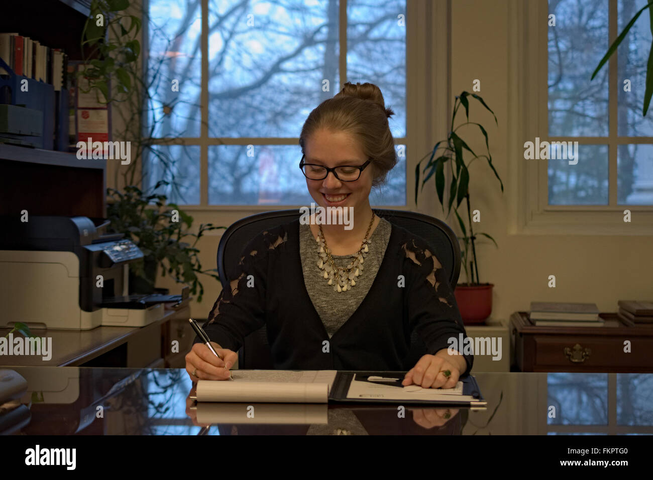 Une jeune femme avec des lunettes est assis derrière un bureau, de l'écriture dans un tampon juridique. Banque D'Images