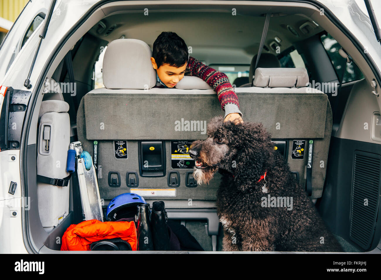 Mixed Race boy petting dog in car hatch Banque D'Images