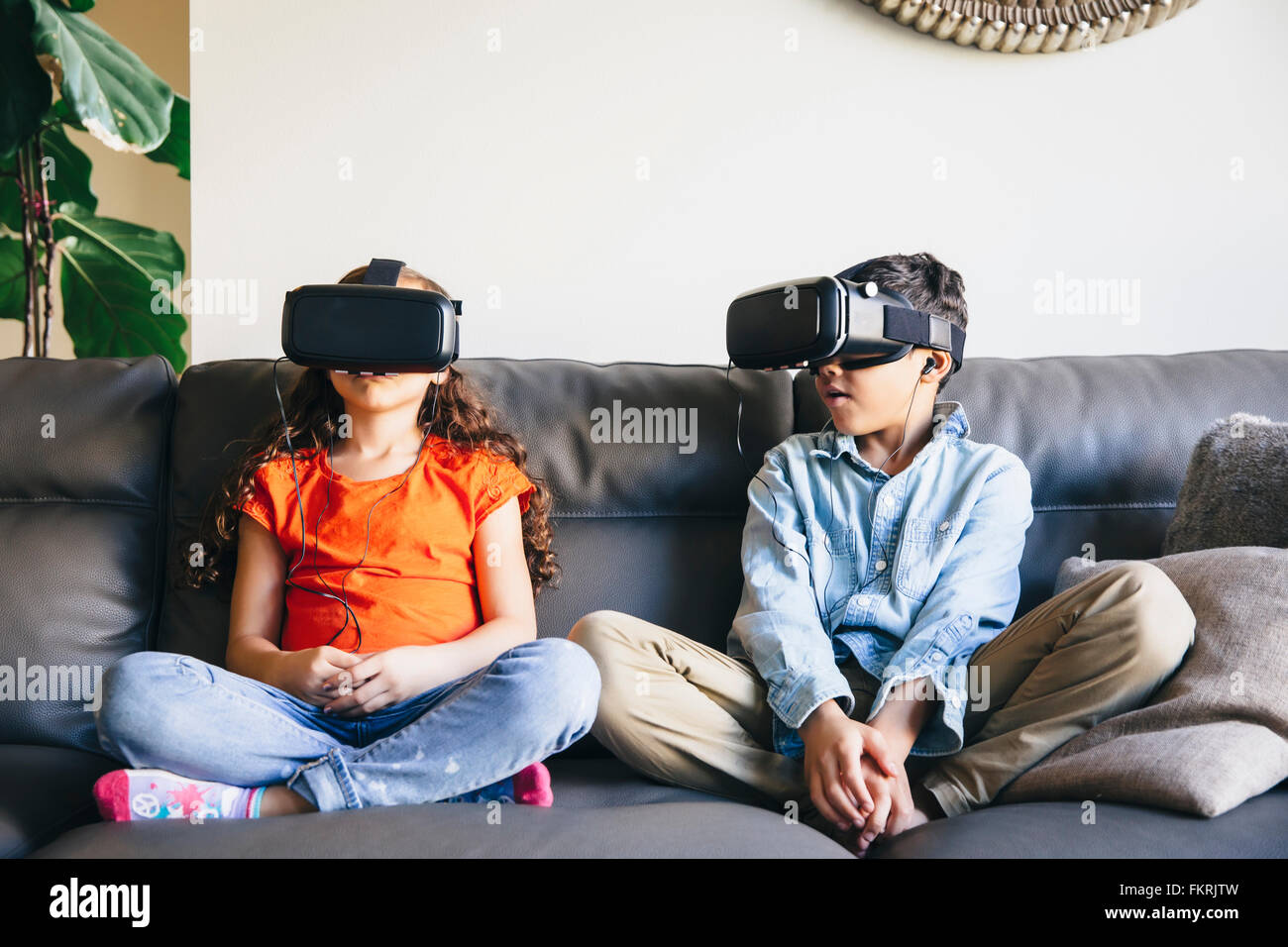 Mixed Race enfants utilisant des lunettes de réalité virtuelle sur canapé Banque D'Images