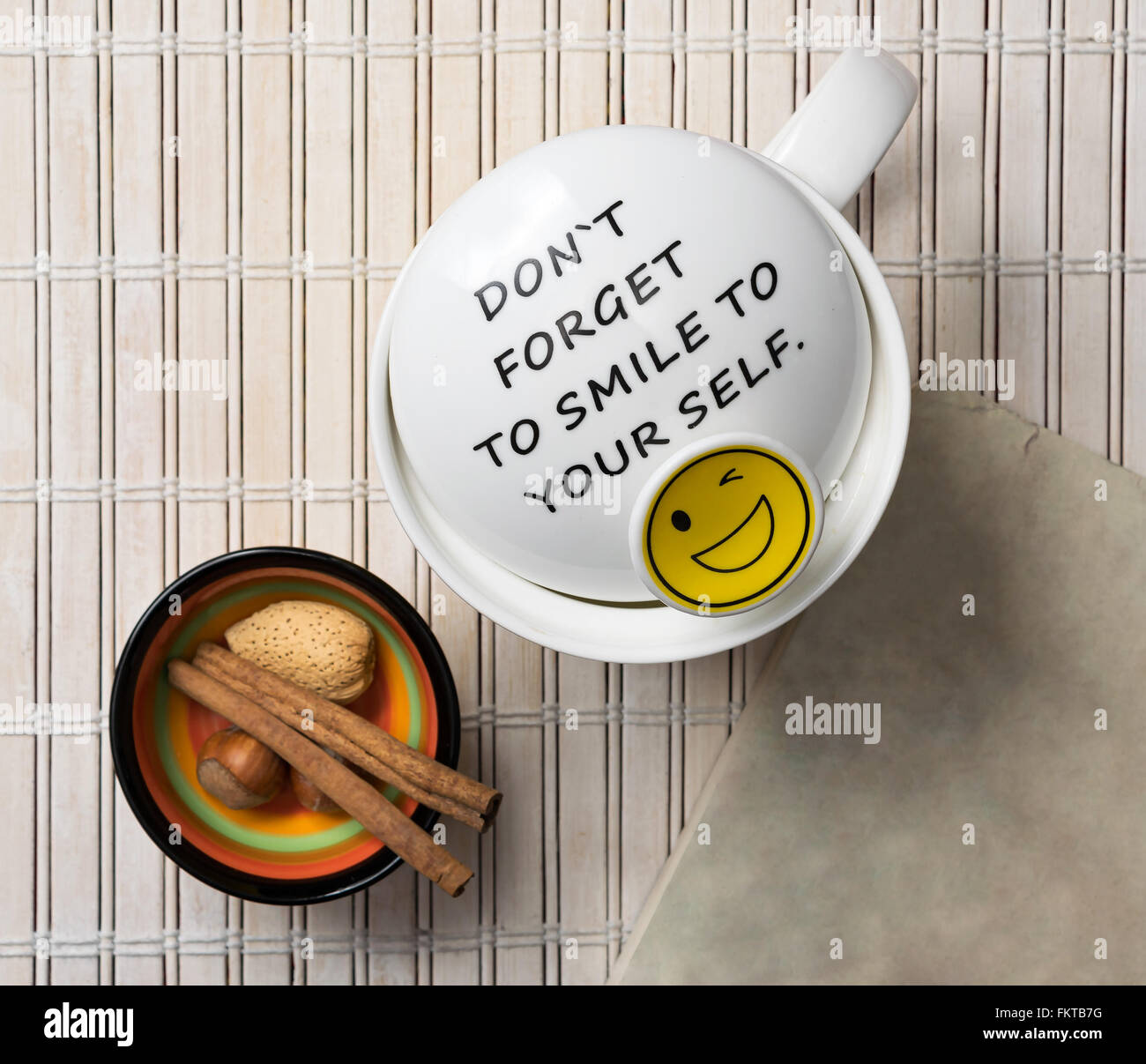 Mug blanc avec une citation positive disant n'oubliez pas de sourire à vous-même et des bâtons de cannelle, de noix, d'amande et de couleur dans un petit Banque D'Images
