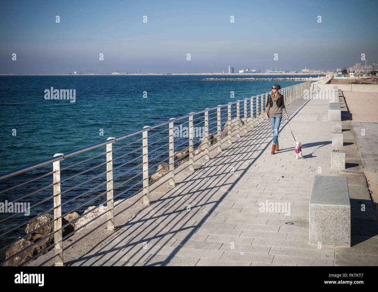Vue avant pleine longueur young woman walking dog sur front de mer à l'écart Banque D'Images