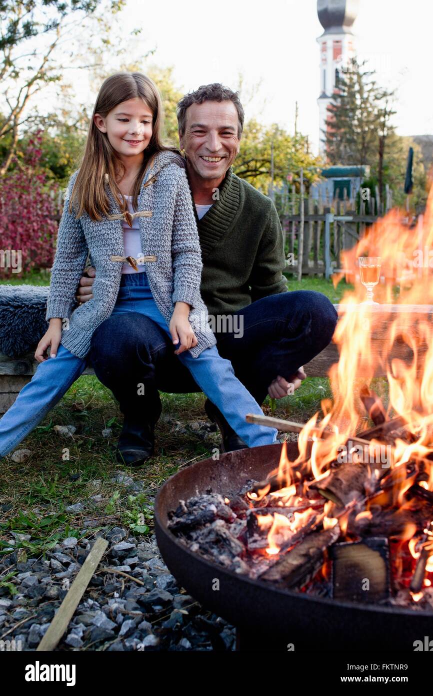 Fille assise sur les genoux du père dans le feu, à regarder le jardin Banque D'Images