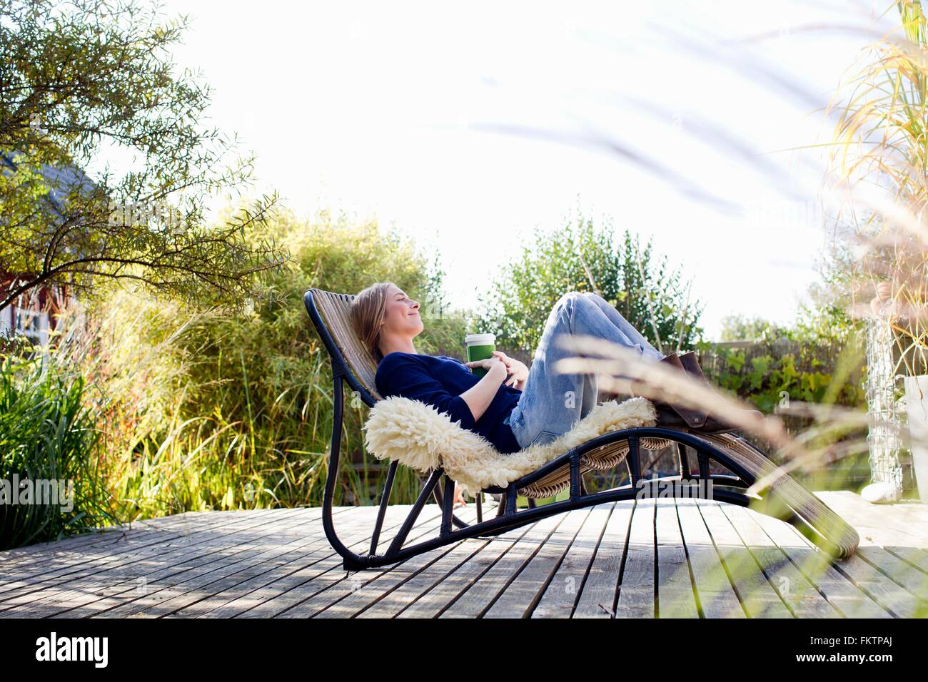 Mid adult woman relaxing on lounge chair on decking en bois Banque D'Images