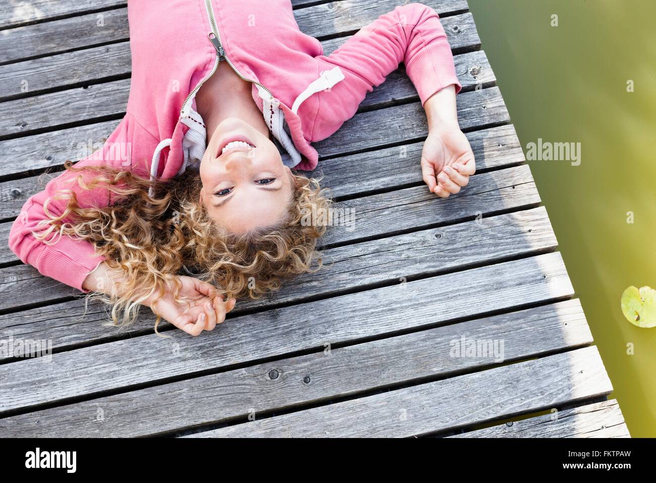 Young woman lying on decking en bois smiling to camera Banque D'Images