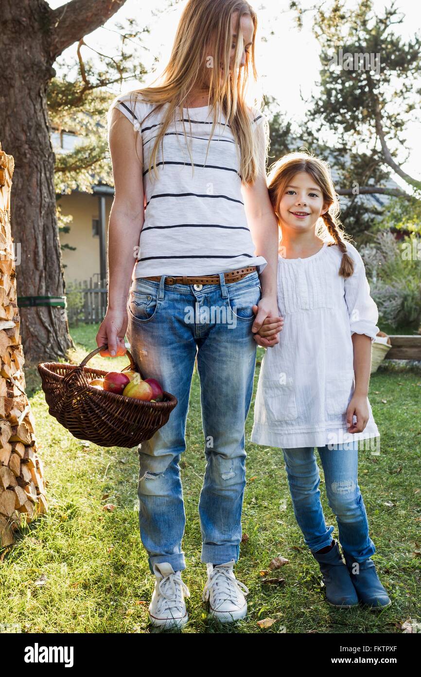 Mère et fille se tenant la main, mère holding basket apples Banque D'Images