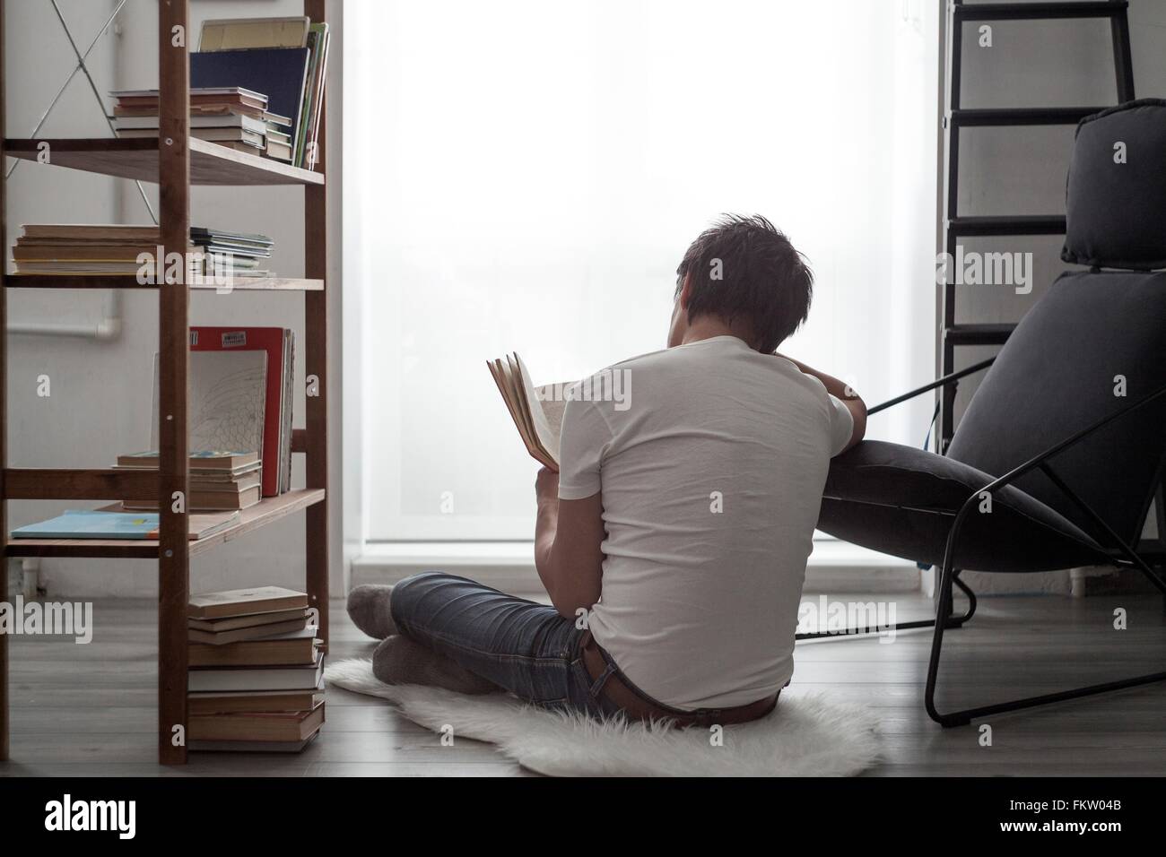 Homme assis sur le plancher du salon en lisant un livre Banque D'Images