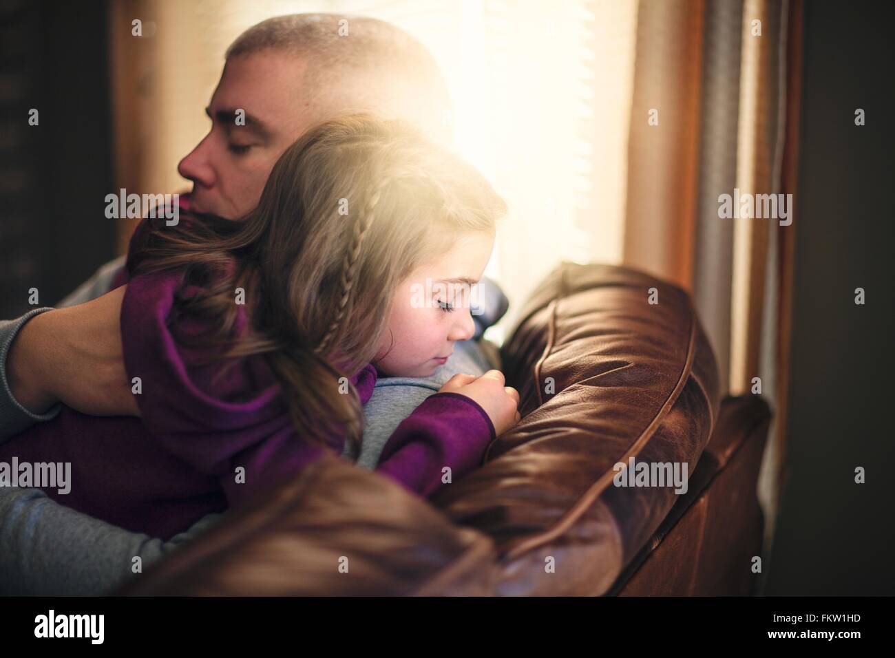Man relaxing on sofa hugging daughter Banque D'Images
