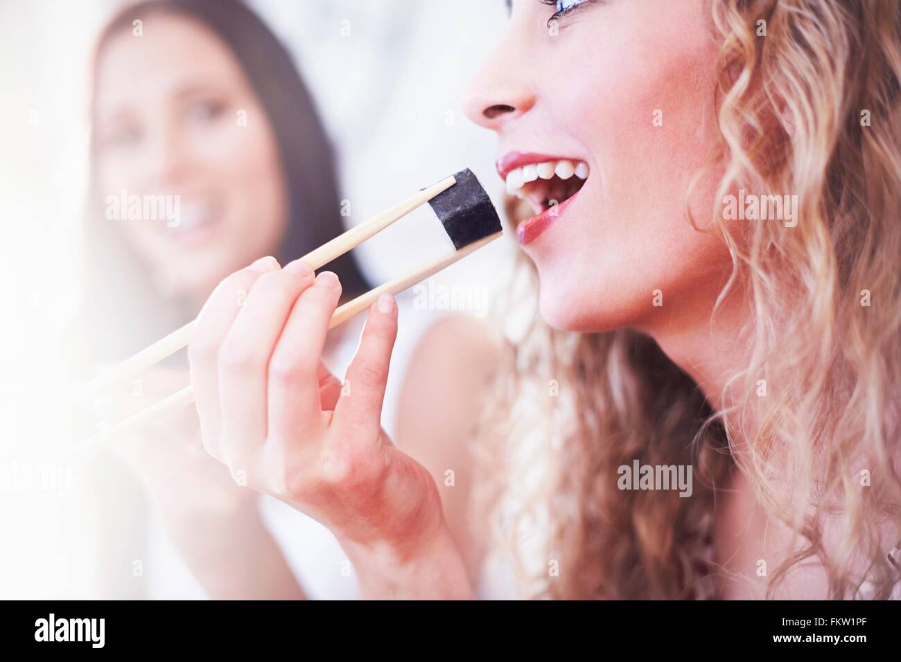 Close up two female friends eating sushi avec des baguettes dans la cuisine Banque D'Images