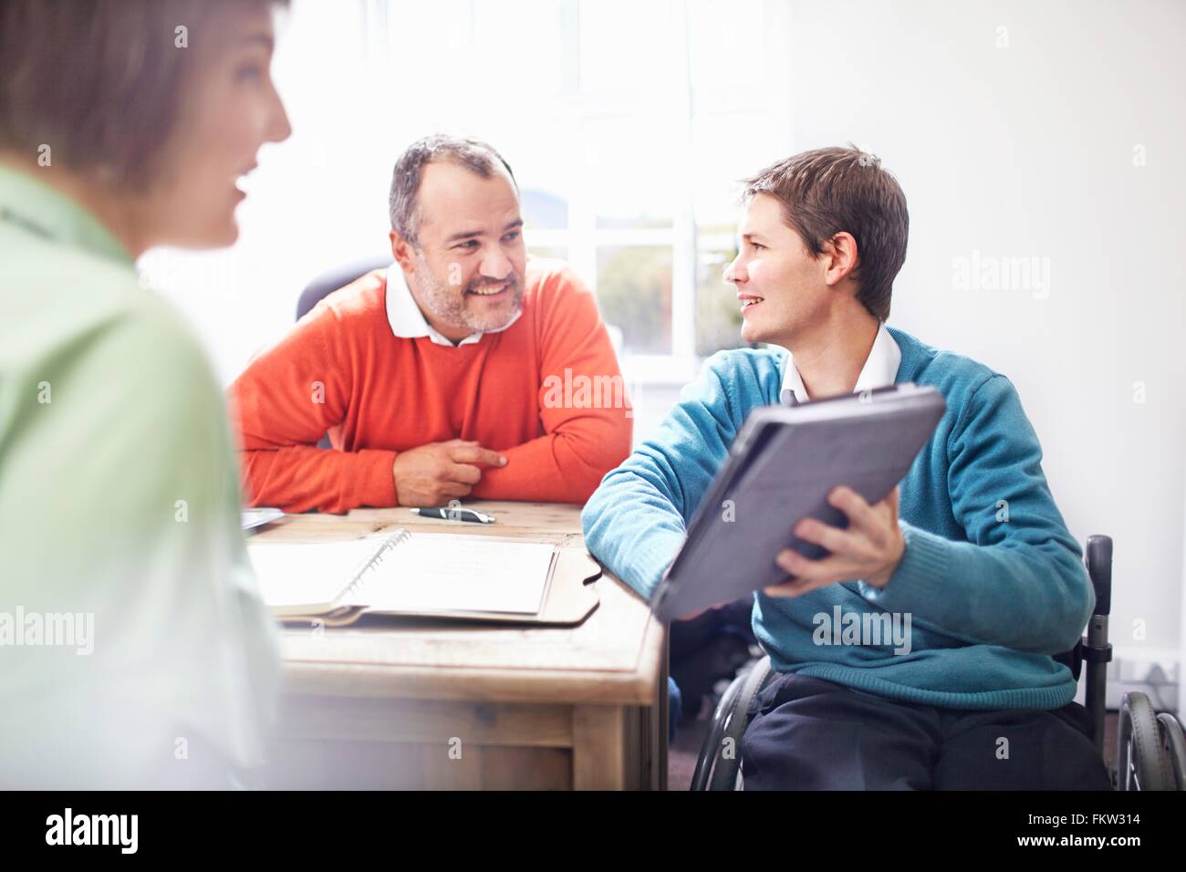L'homme en fauteuil roulant dans office montrant collègues digital tablet, smiling Banque D'Images