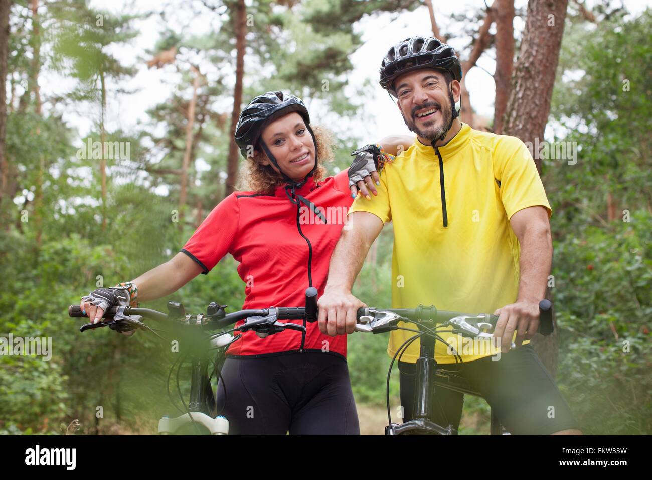 Portrait happy mountain biking couple in forest Banque D'Images