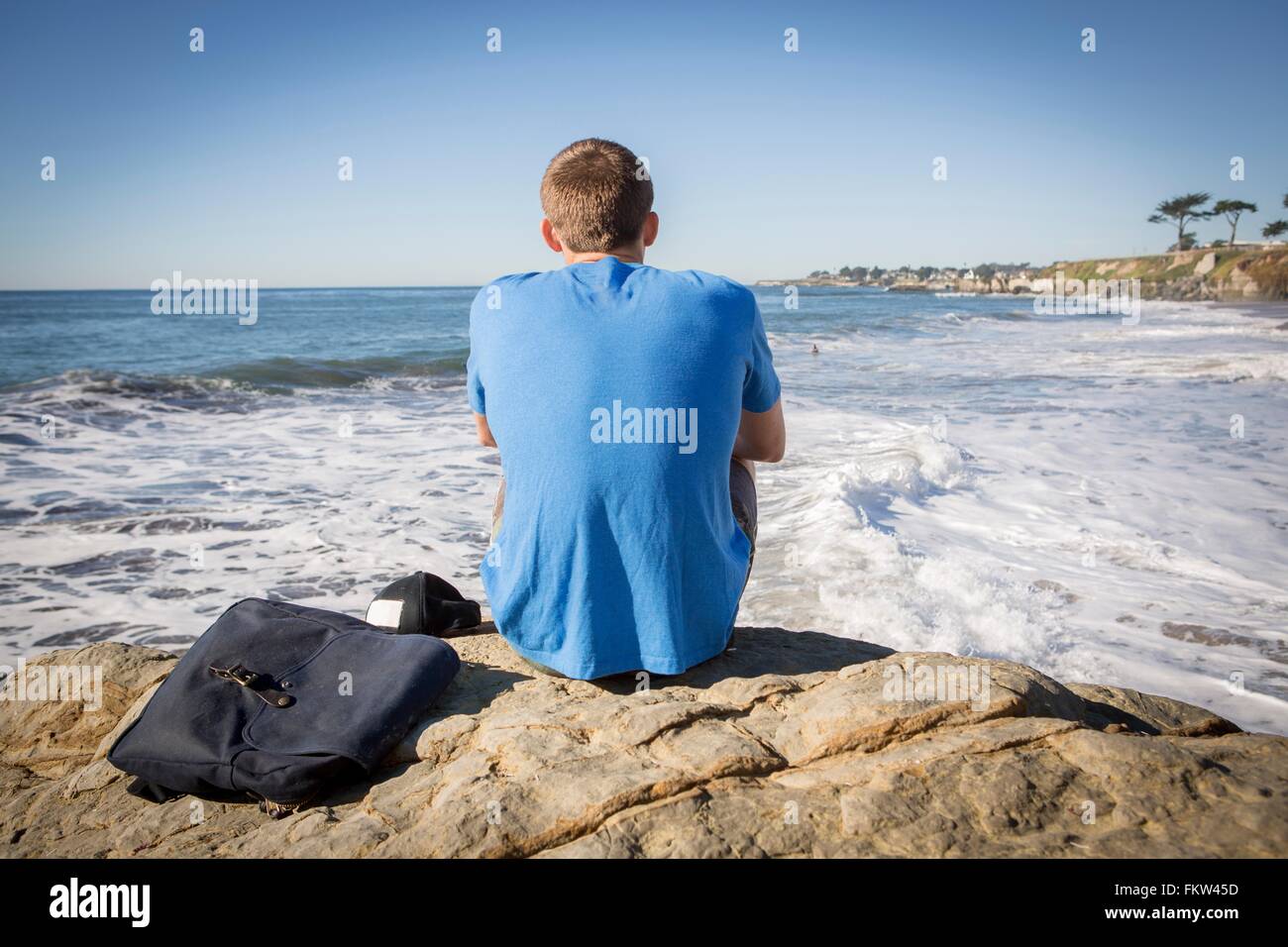 Jeune homme assis par Roche, surplombant la mer, vue arrière Banque D'Images