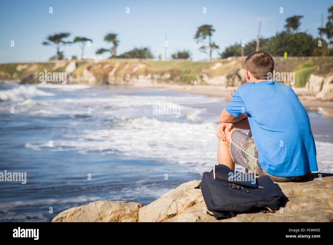 Jeune homme assis par Roche, surplombant la mer, vue arrière Banque D'Images