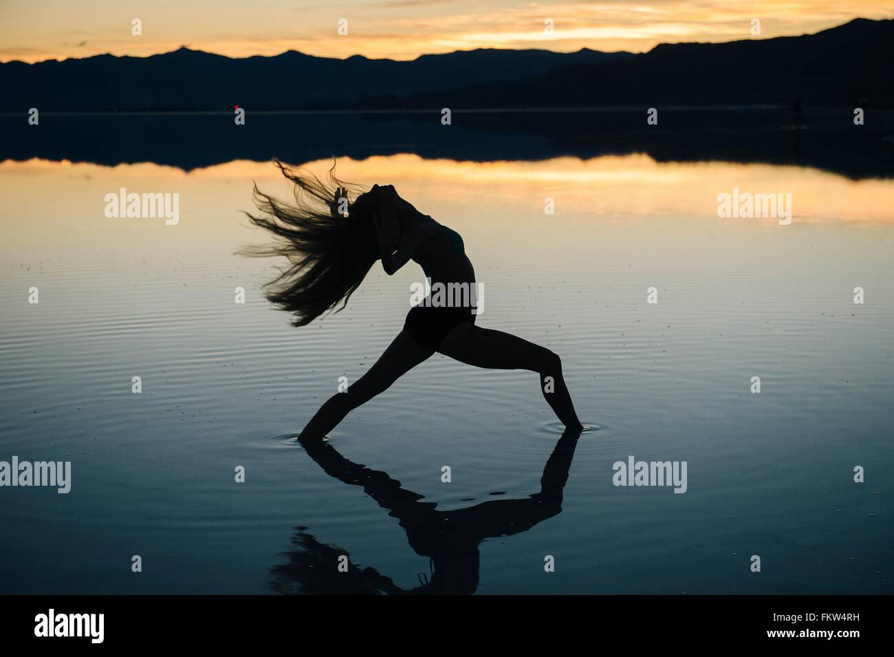 La silhouette danseuse jetant en arrière ses longs cheveux dans le lac au coucher du soleil, Bonneville Salt Flats, Utah, USA Banque D'Images