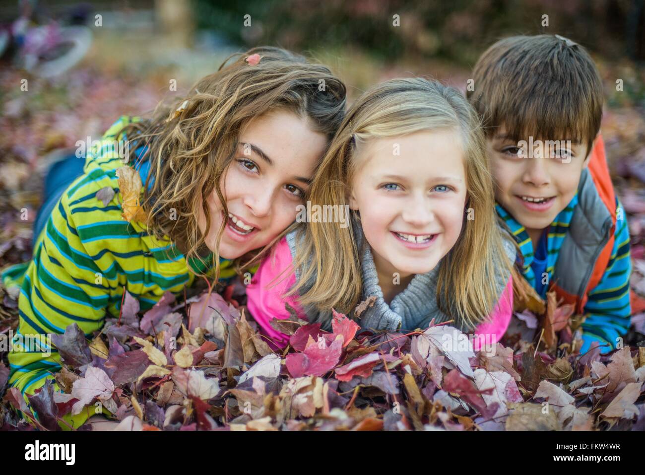 Les enfants couchés sur les feuilles d'automne au jardin Banque D'Images