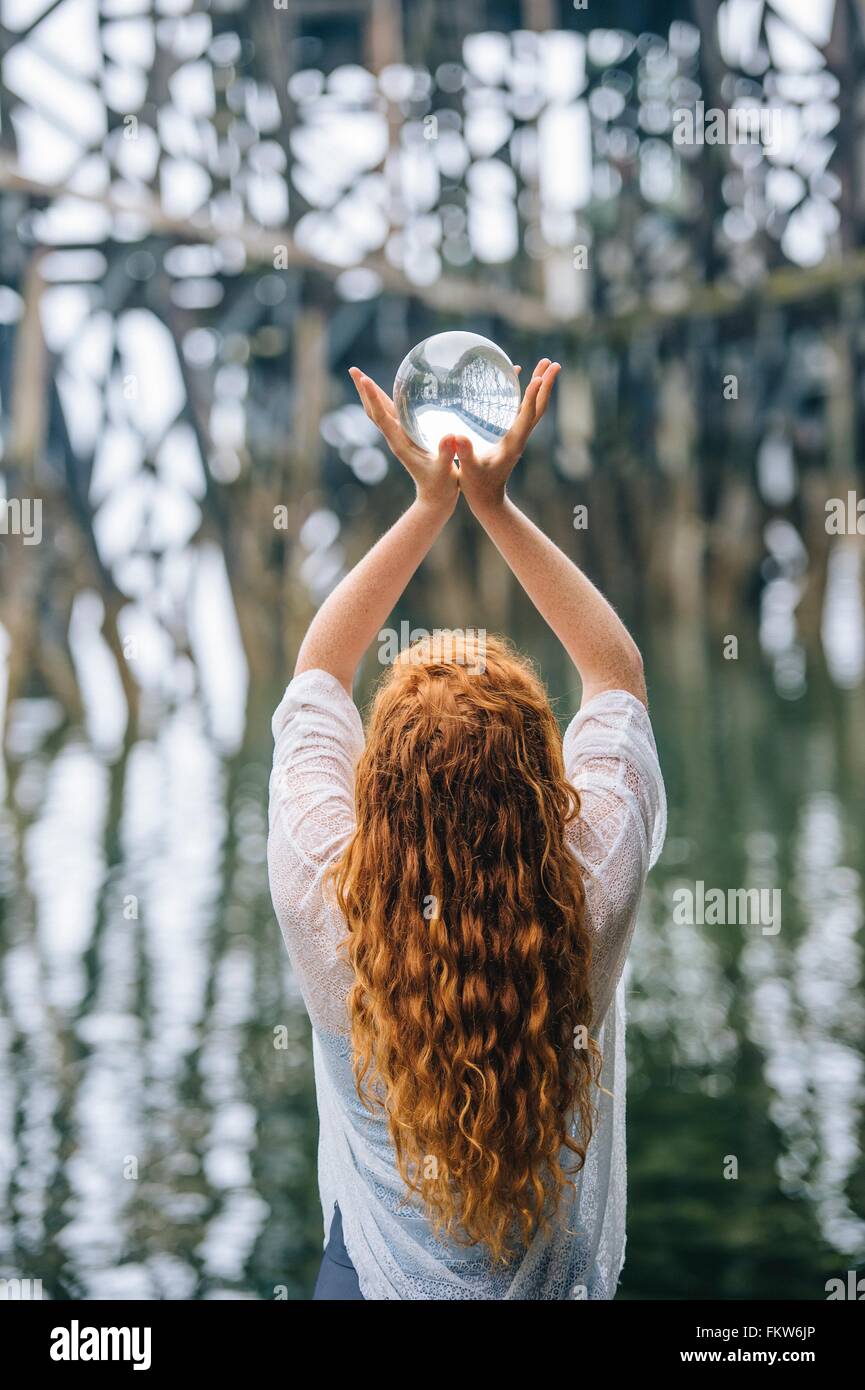 Rear view of woman holding up boule de cristal en face de wood river pier Banque D'Images
