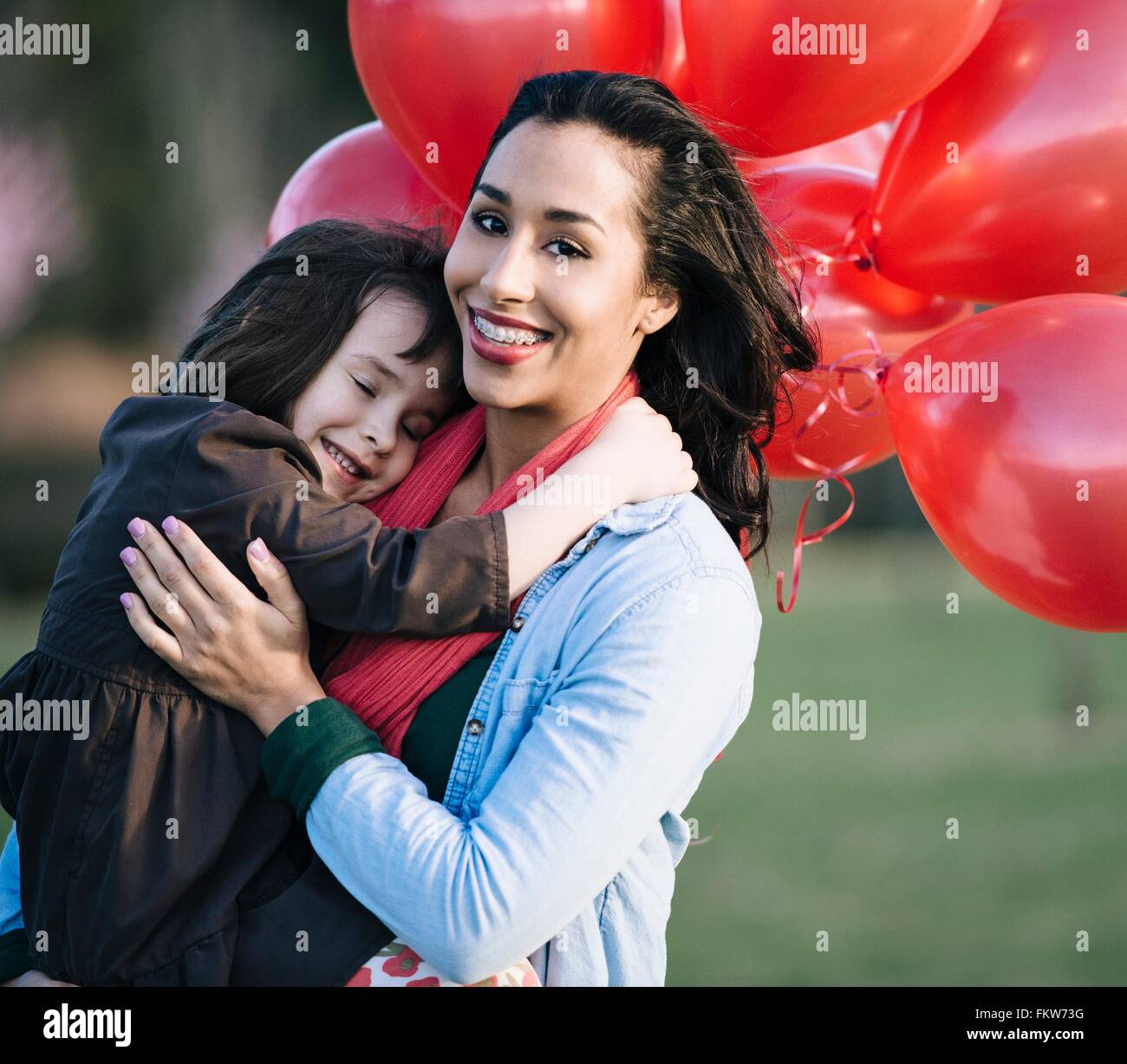 Portrait of Girl with bunch of red balloons hugging mother in park Banque D'Images