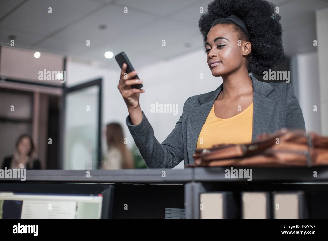 Young businesswoman reading text à la réception bureau smartphone Banque D'Images