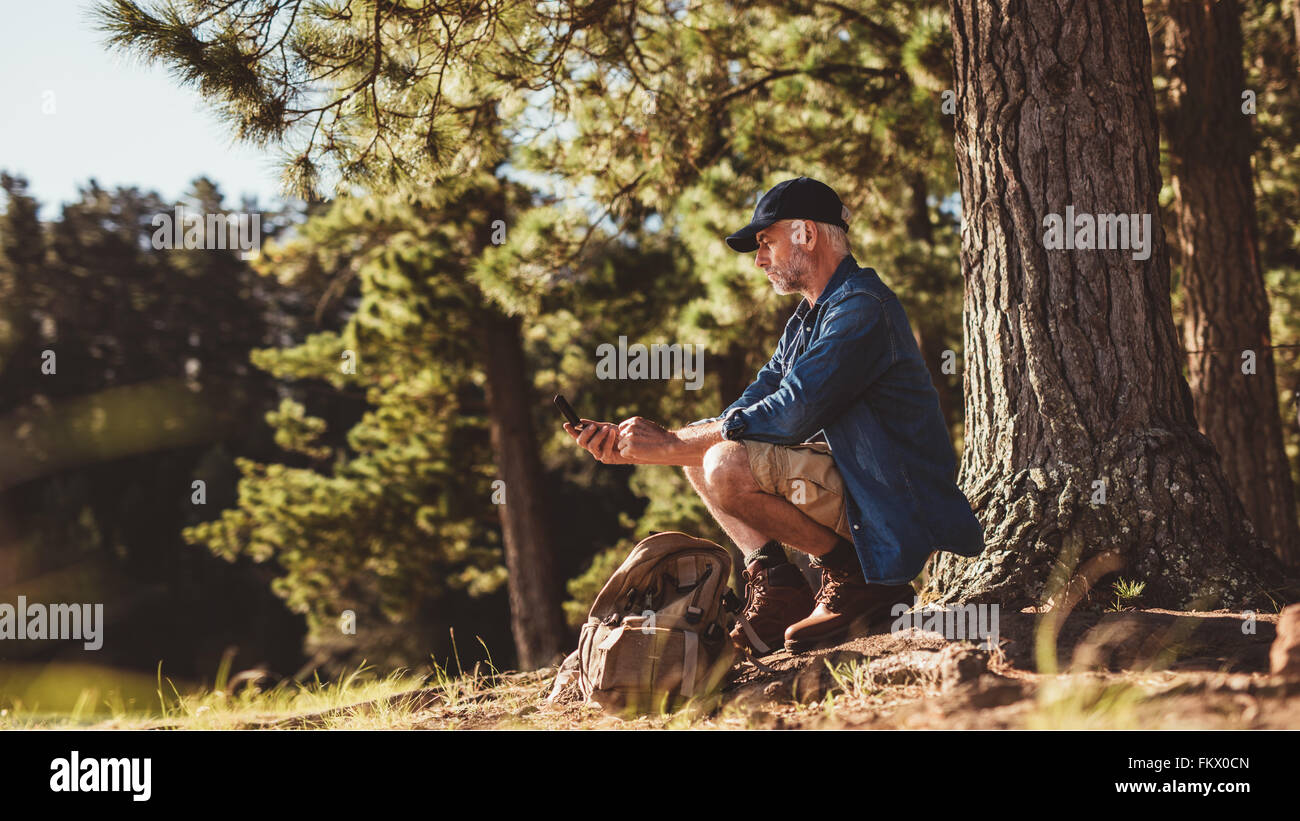 Young hiker assis par un arbre dans la forêt et contrôler sa position à l'aide d'une boussole. Man sur la randonnée dans la nature à l'aide d'un Banque D'Images