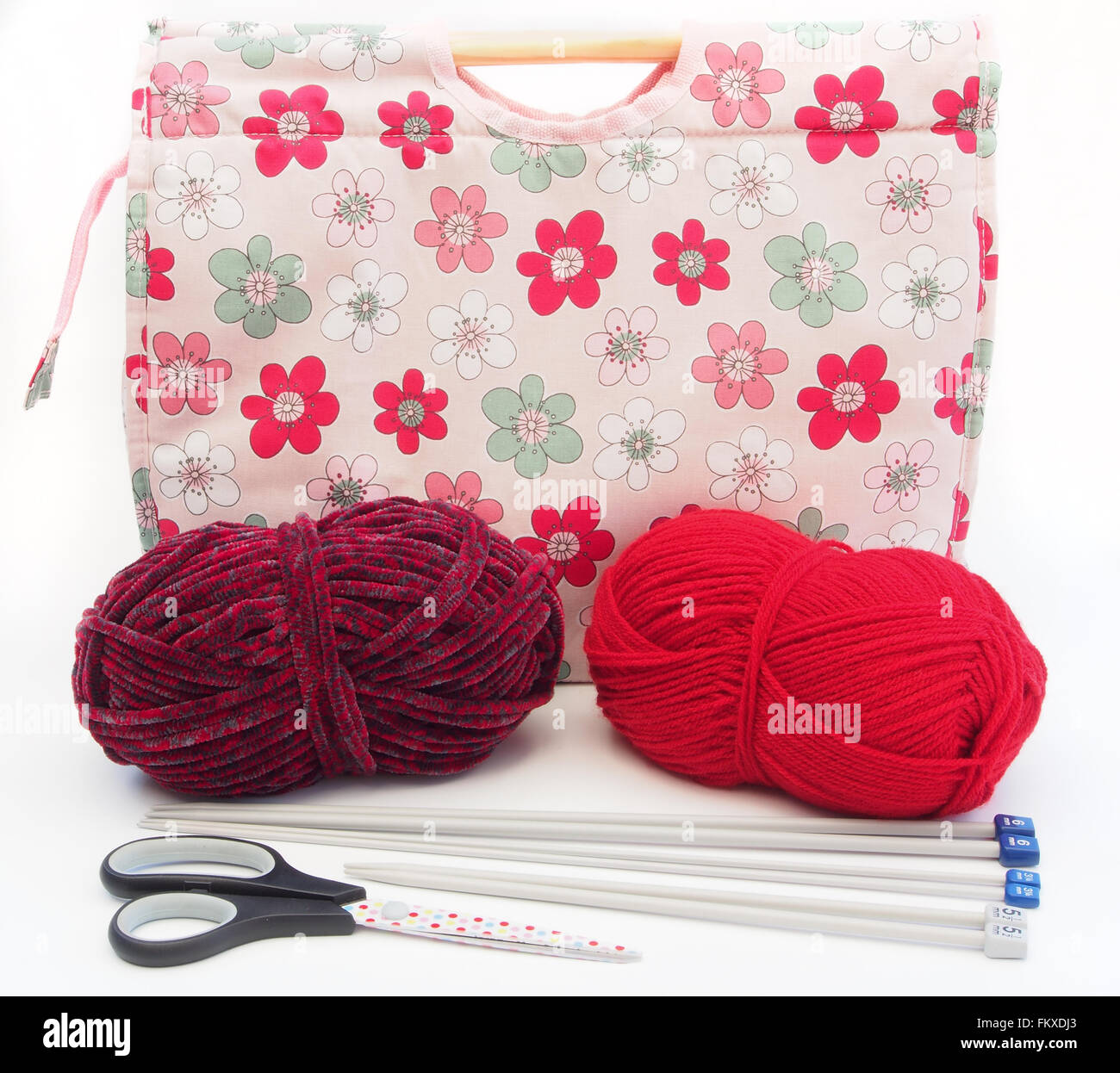 Tricot à motifs fleurs rose / artisanat sac avec des aiguilles à tricoter, laine rouge et bourgogne et ciseaux sur un fond blanc. Banque D'Images