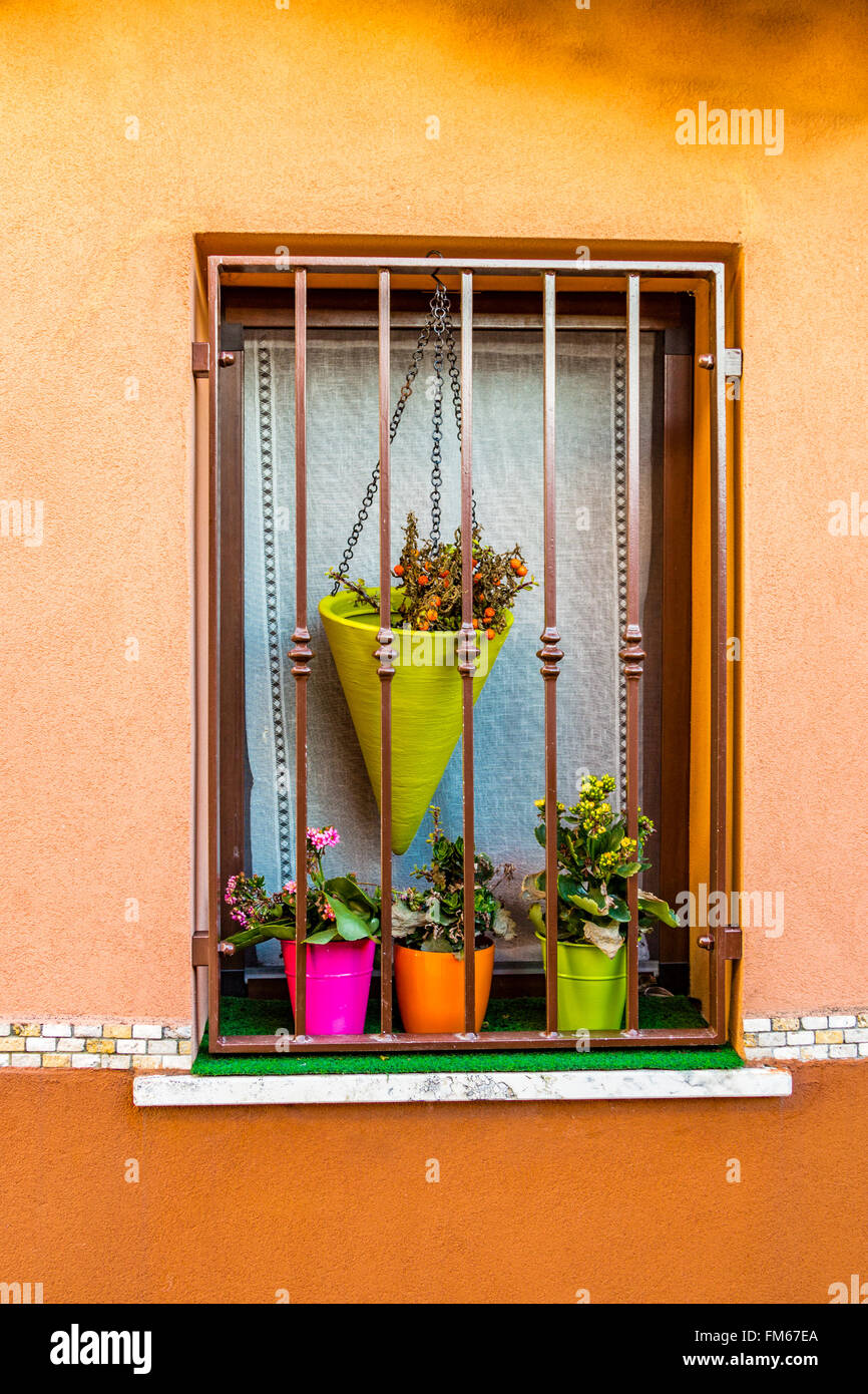 Fenêtre avec grille en fer et fuchsia, orange et vert pots de fleurs Banque D'Images