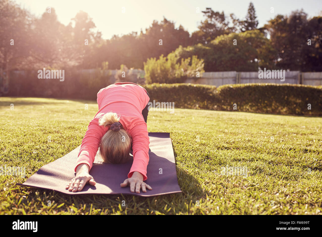 Woman in yoga pose sur tapis en plein air avec sunflare Banque D'Images