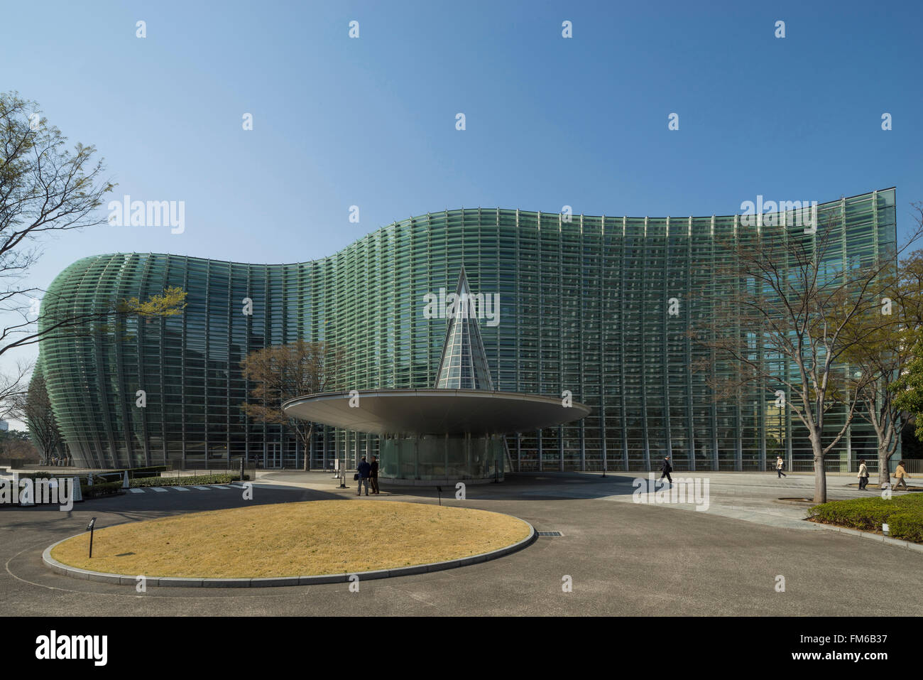 Un grand bâtiment de verre courbé, avec un œil en forme de disque de capture de l'auvent en acier à partir de laquelle un triangle de verre se lève, est l'entrée de Tokyo, du Centre national des Arts, avec des gens qui marchent sur les jardins paysagers. Banque D'Images