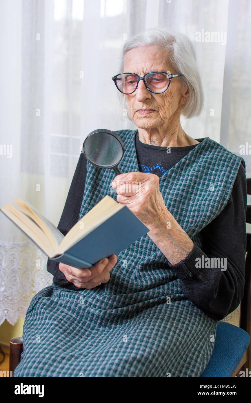 Quatre-vingt-dix ans grand-mère la lecture d'un livre par loupe Banque D'Images