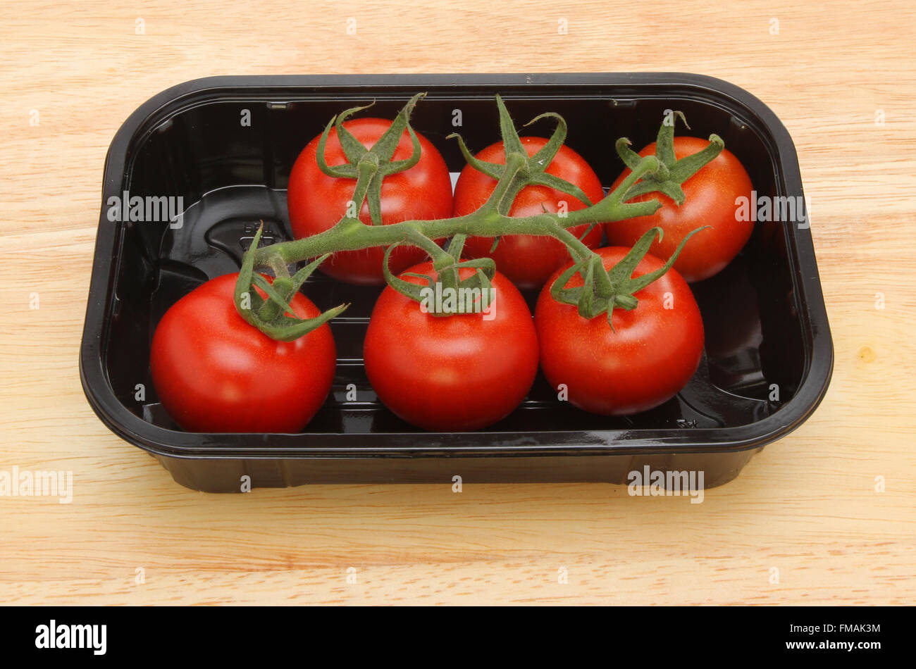 Vigne tomates mûries dans un bac en plastique noir sur une planche en bois Banque D'Images