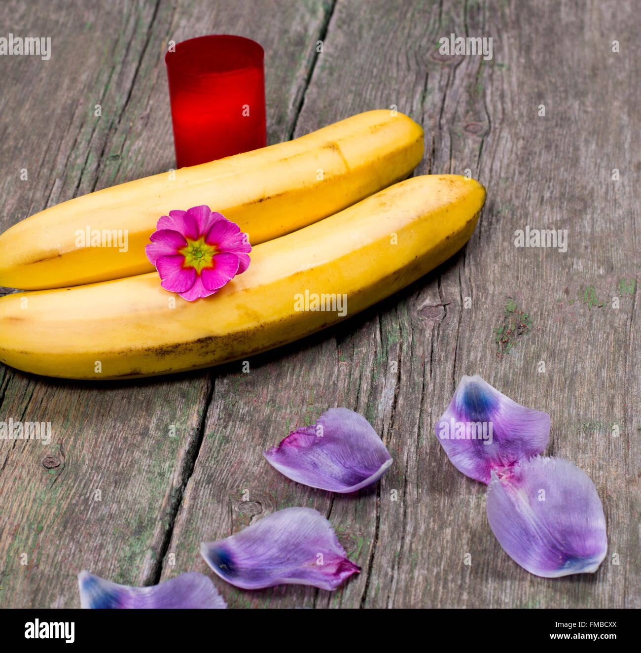 Bougie, deux bananes, fleurs et pétales de lilas Banque D'Images