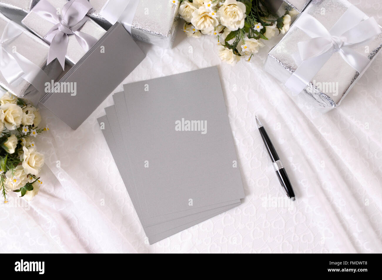 Argent gris papier d'écriture ou des invitations avec enveloppes posées sur bustier dentelle avec plusieurs cadeaux de mariage et de bouquets de roses blanches. Banque D'Images Argent gris papier d'écriture ou des invitations avec enveloppes posées sur bustier dentelle avec plusieurs cadeaux de mariage et de bouquets de roses blanches. Banque D'Images