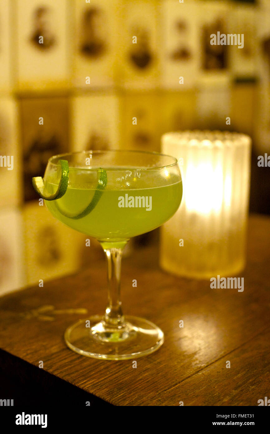 Un cocktail vert est situé sur une barre en bois haut avec une bougie brûlant dans l'arrière-plan. Banque D'Images