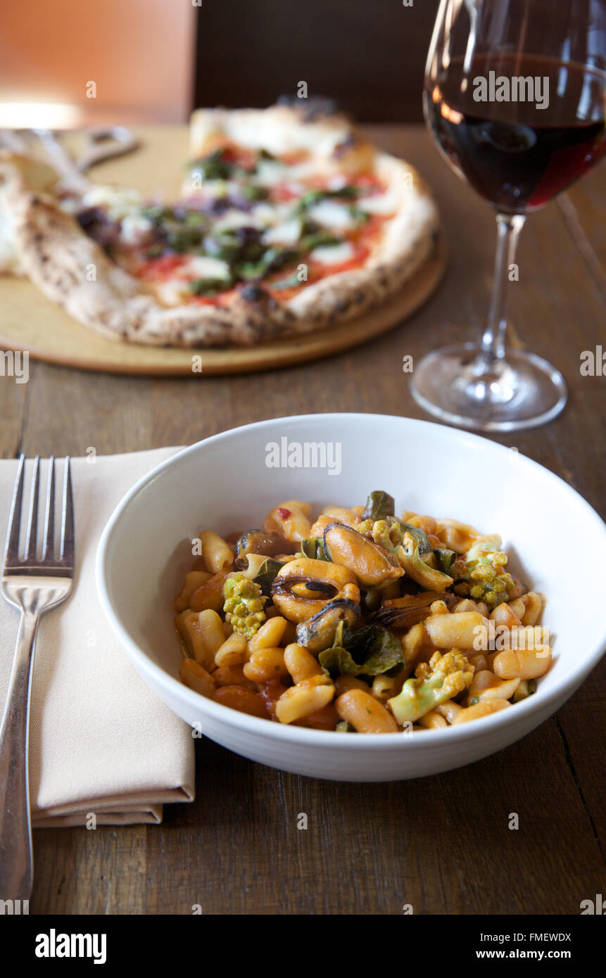 Un bol de haricot blanc, romanesco et les moules soupe avec du vin rouge et une pizza sur la table derrière elle. Banque D'Images