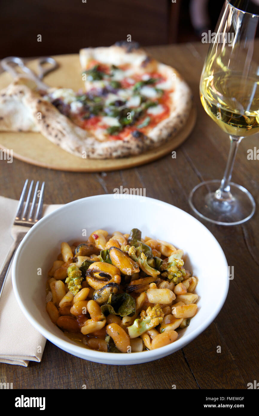 Un bol de haricot blanc, romanesco et les moules au vin blanc soupe et une pizza sur la table derrière elle. Banque D'Images
