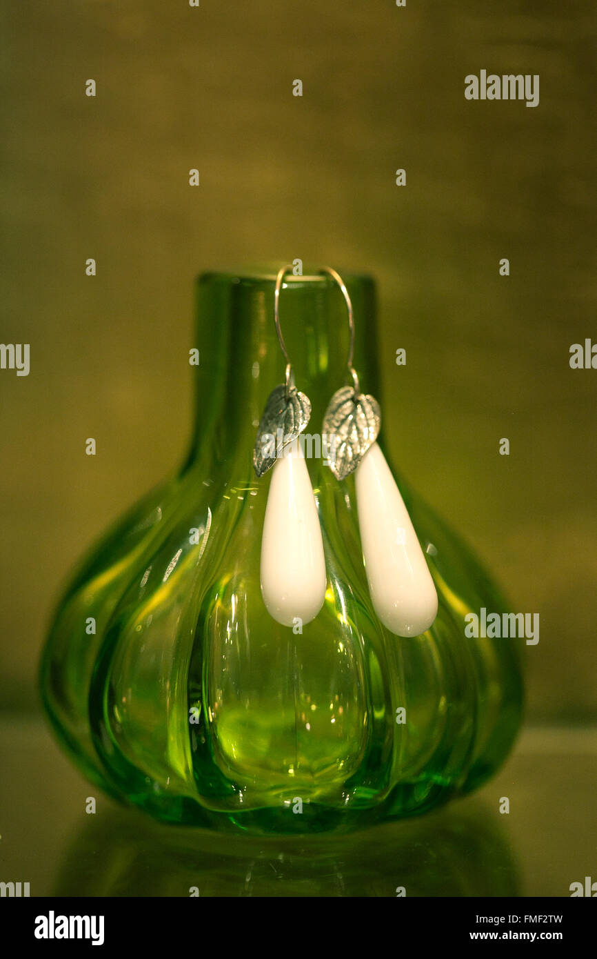 Gros plan d'une paire de boucles d'accroché sur un petit vase en verre de couleur verte. Banque D'Images