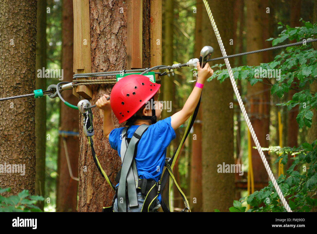 Un garçon la corde de sécurité crochets pour un nouveau fil dans un parcours de corde Banque D'Images